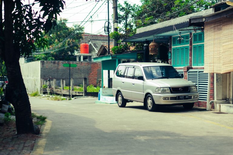 A serene urban street scene with a parked car and colorful houses under a clear sky.